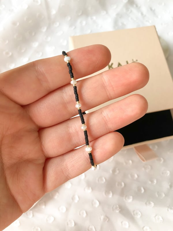 Pleciona czarna bransoletka z jedną perełką i złotymi koralikami