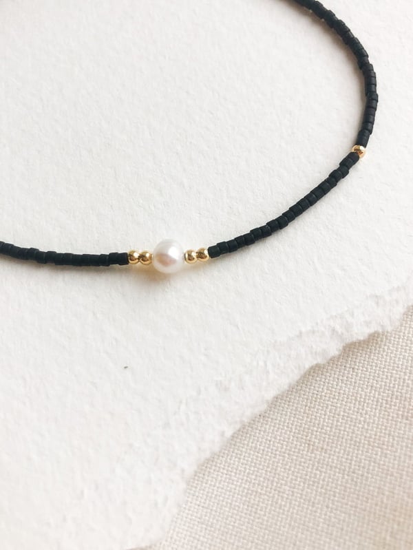 Pleciona czarna bransoletka z jedną perełką i złotymi koralikami